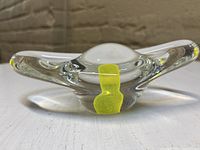 Front view of clear glass egg-shaped paperweight with yellow yolk visible inside base, smooth clear glass surface on table.