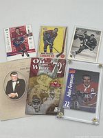 Overview photo showing four hockey cards, 1972 Team Canada souvenir card, obituary celebration of life card and one signed card in protective case