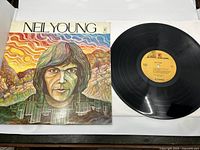 Front cover of the Neil Young 1969 self-titled LP showing the colorful painted portrait artwork beside the black vinyl record with an orange-yellow label.