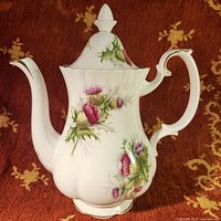 Front side view of Royal Albert Highland Thistle porcelain teapot on red patterned fabric.