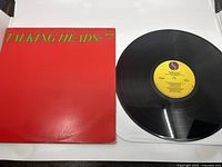 Photo showing the front cover of Talking Heads: 77 album alongside the vinyl disc with yellow Sire Records label.