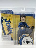 Front view of sealed John Lennon McFarlane Toys 2004 figure in packaging showing figure and branding.