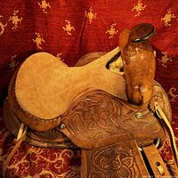 Side angle view of the vintage child's western saddle showing the suede seat, floral tooled leather fender, and saddle horn.