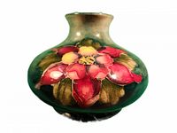 Front view of Moorcroft vase showing large floral design with purple, pink, yellow Columbine flowers and green leaves on green background.