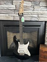 Full front view of black Yamaha Pacifica guitar on stand in front of fireplace