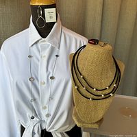 Photo showing a white shirt form displaying a long silver-tone chain necklace with crystals, a pair of hoop earrings, and a black bust displaying a black leather multi-strand choker necklace with metal beads, a red rubber ring with a red stone, and a silver-tone pendant