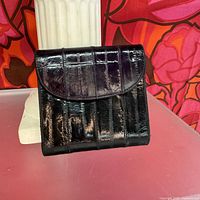 Front view of the black wallet showing vertical banded eel skin texture with slight purple sheen.