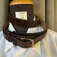 Dark brown leather belt coiled and placed on a mannequin with white shirt, showing belt buckle and strap condition.