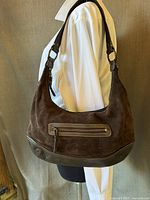 Side view of brown suede Eddie Bauer hobo purse on mannequin, showing suede body and leather bottom edge with zippered front pocket.