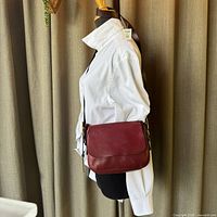 Side profile of the maroon leather crossbody bag worn on a mannequin modeling white shirt.