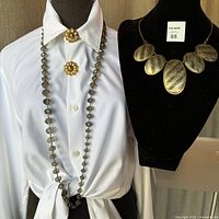 Four piece vintage jewelry lot on display, including a long smokey faceted glass Kenneth Cole necklace with dark translucent beads, paired with gold flower-shaped vintage clip-on earrings attached to shirt collar, and another mixed metal brutalist necklace on black bust.
