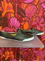 Side view of the pair of dark brown leather Frye Melanie slip-on shoes with white rubber soles against a colorful background.