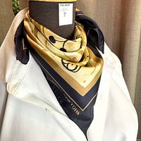 Scarf styled on a dress form showing navy border and gardening motif in gold and tan on silk fabric.