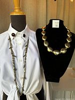 Photo showing two necklaces displayed on a mannequin and black necklace stand: one long feather chain necklace on the mannequin and one gold tone nugget bead necklace on the necklace stand.