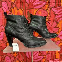 Side view of both black leather ankle boots on display stand showing textured leather and heel height