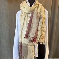 Cream pashmina shawl with cream embroidery and maroon-gold bordered fringed ends displayed on mannequin and hung showing detail of weave and embroidery.