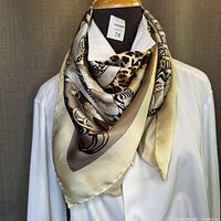 Silk scarf worn over white shirt showing leopard, zebra, and chain print with cream border.