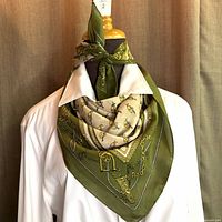 Scarf tied around mannequin neck showing green and cream sections with equestrian chain and stirrup motifs.