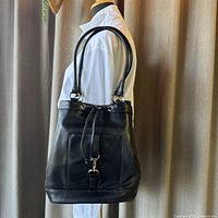 Side profile of Talbots black leather bucket shoulder bag on mannequin, showing the shoulder straps and overall shape.