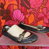 Side view of UGG Gerty Mary Jane ballet flats showing dark brown leather with metallic bronze strap and buckle, fabric shoe form inside one shoe.