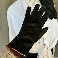 View of the palm side of one black suede glove showing the smooth suede material and tan leather trim at the wrist edge, size tag visible inside.