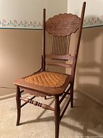 Full view of antique carved oak chair showing spindle back, cushioned seat with nail head trim, turned legs and stretchers