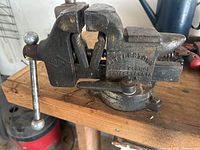 Side view of the bench vise mounted on a wooden surface showing the vise jaw and swivel base.
