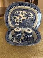 Full set showing square oval bowl, plate as backdrop, and salt and pepper shakers inside bowl.
