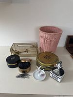 Overall group of boudoir and bath treasures showing woven basket, trays, tins, porcelain figurines, and hairpins.