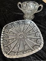 Photo showing both EAPG pieces, the square platter and two-handled pedestal bowl, on a black background to highlight patterns and shapes.