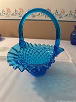 Blue hobnail glass basket with ruffled edge and arched handle, showing side angle and textured glass pattern.