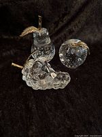 Front view of all three glass fruit paperweights (pear, apple, grape) on black fabric background showing detail of bubbles and brass stems/leaves.