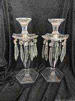 Pair of clear crystal candelabra with hexagonal bases and hanging prisms shown against a black background.