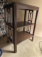 Three photos showing a small wooden lamp table with mahogany veneer, fluted decorative legs, and carved geometric side panels. The table has three surfaces: top, middle, and bottom shelves, suitable for display or storage. Dimensions noted as 18"w x 12"d x 25"h.