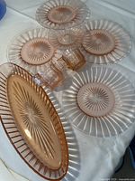 Pink Heisey glass set on white fabric showing four 7-1/2 inch plates, one smaller 4-3/4 inch plate, creamer, sugar bowl, and 12 inch oval bowl