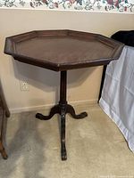 Side view of the octagonal pie crust table showing the carved edge along the top surface and the three carved clawfoot legs on the pedestal base.
