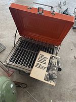 Vintage Zebco tabletop gas grill open showing grill grate and original pamphlet