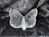 Front-facing photo of a clear crystal butterfly figurine with a textured wing pattern and a Waterford sticker on the right wing, placed on a black fabric background.