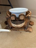 Full view of wooden frog planter holding white stoneware pot, showing frog's face and details with plastic watering can nearby.