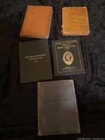 Photo of all 5 US Army military manuals laid out on black fabric showing varied cover conditions from well used to worn and split bindings