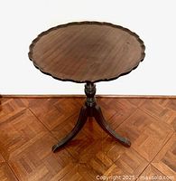 Front view of the vintage piecrust table showing the full pedestal and three spider-style legs on parquet flooring.
