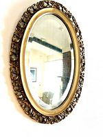 Frontal view of the vintage oval mirror showing ornate gold carved frame and reflective mirror surface.