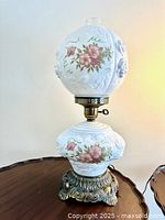 Full view of vintage parlor lamp with milky glass globe and reservoir featuring pink wild rose floral pattern, ornate brass base, and clear chimney