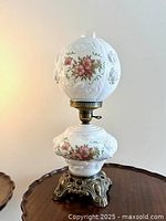 Full view of vintage parlor lamp with spherical milk glass shade and embossed floral wild rose decal pattern, showing brass burner and ornate brass base.