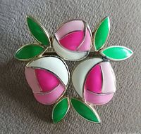 Front view of the flower-shaped brooch with pink, purple, white enamel petals and green enamel leaves. Gold-tone metal base.