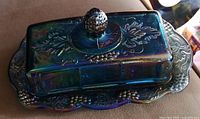 Butter dish with lid showing grape cluster handle and embossed grape and leaf patterns on top and sides.