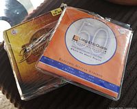 Two packed guitar strings, Long & McQuade electric guitar strings in orange packaging and Dean Markley Vintage Bronze acoustic strings with yellow packaging, both wrapped in plastic.