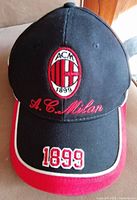 Front view of black and red baseball cap with embroidered AC Milan crest and 1899 on brim.