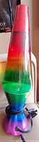Full photo of the rainbow retro lava lamp showing the colorful liquid in the glass container and the metallic rainbow base and cap.