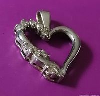 Heart-shaped pendant photographed on a purple background, showing diamond-detail side and the 10K white gold stamp on the back side.